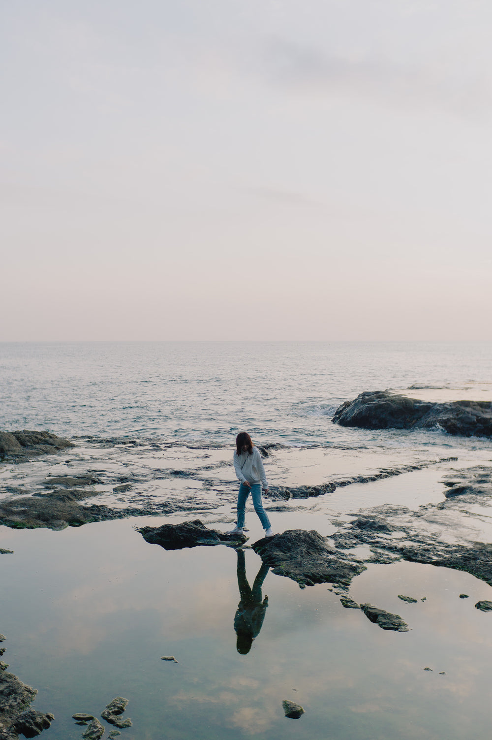 person-stands-on-rocks-poking-out-of-the-ocean-shoreline